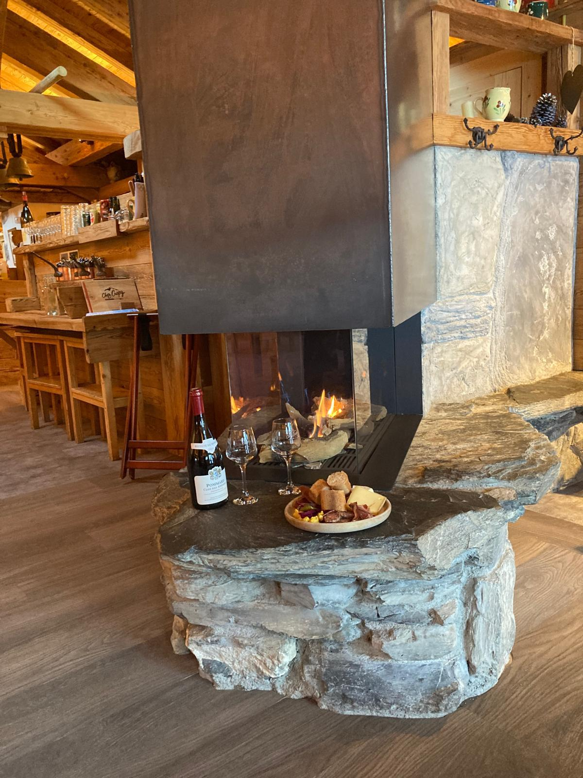 Cheminée en pierre du chalet Chez Crépy, verre de vin et plateau au coin du feu